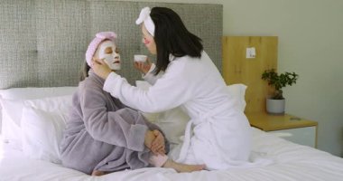 Çinli anne ve kız fırçalarını kaseye daldırıyorlar, yüz maskesi takıyorlar, yatakta selfie çekiyorlar. Aile, cilt bakımı, kaynaşma, rahatlama, konforlu, samimi, sağlıklı.