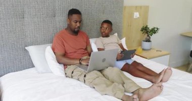 Afro-Amerikan ailesi, bilgisayarlarını kapatıp meyve suyu almadan önce tablete bakıp gülümsüyor. Aile, bağ, eğlence, teknoloji, rahatlama, konfor, bağlantı