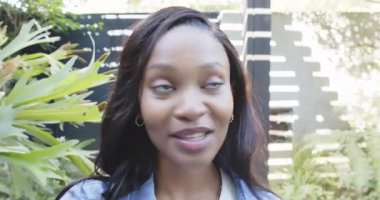 Afro-Amerikalı bir kadın kendini bahçe avlusunda tanıtıyor elinde akıllı bir telefonla koridora çıkıyor. Açık hava, teknoloji, yaşam tarzı, modern, iletişim, refah, doğal