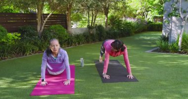 Asyalı Çinli eğitmen, yaşlı kadına bahçede hasırların üzerinde kalas sallayarak, katlanarak, gülümseyerek rehberlik ediyor. Sağlık, zindelik, açık hava, sükunet, canlılık, etkinlik, uyum.