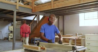 Siyahi erkek stajyer, atölyedeki testere tezgahına tam isabetini gösteren eğitmen üstüne testere. Atölye, marangozluk, işçilik, güvenlik, akıl hocalığı, kılavuz, endüstri