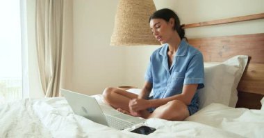 Pijamalı bir kadın yatakta dizüstü bilgisayar kullanıyor, evde sabah rutininin tadını çıkarıyor. Yaşam tarzı, eğlence, teknoloji, rahatlama, rahat, rahat