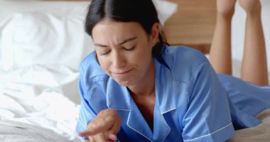 Mavi pijamalı bir kadın yatakta uzanıyor, gülümsüyor ve evde sabah rahatlığının tadını çıkarıyor. Yaşam tarzı, sabah rutini, mutluluk, rahatlık, huzur, sükunet.