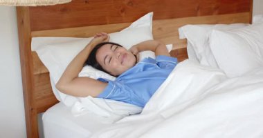 Uyanan, yatakta esneyen mavi pijamalı bir kadın, kendini iyi hisseden, evinde. Sabah, rahatlama, yatak odası, sağlık, uyanma, rahatlık.