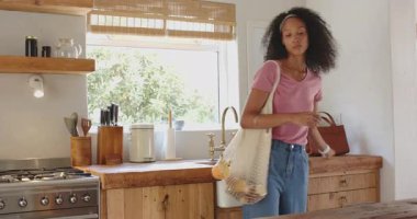 Kadın evde, kırsal mutfakta yeniden kullanılabilir poşetlerde taze meyve düzenliyor. Sürdürülebilirlik, çevre dostu, sıfır atık, bakkaliye, organik, ev