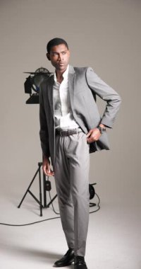 Dikey video: Gri takımlı kendine güvenen adam moda stüdyosunda profesyonel ışıklandırmayla poz veriyor. stil, zarafet, erkek giyim, sofistike, portre, modellik