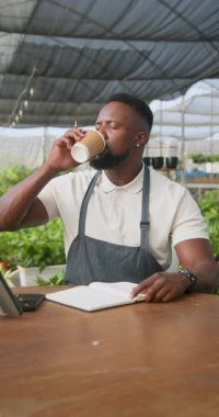 Dikey video: Afro-Amerikalı bir adam serada notlar yazıyor, bitki bakımına odaklanıyor. Bahçıvanlık, bahçıvanlık, tarım, sürdürülebilirlik, botanikçi, çevre
