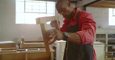 Afro-Amerikalı bir adam çerçeveyi zımparalıyor sonra da pürüzsüz bir son için tezgahın önüne zımparalıyor. Sanatçı, marangozluk, işçilik, atölye, mobilya, marangozluk, el işçiliği