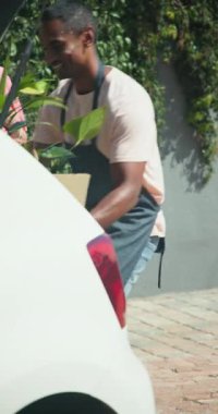 Dikey video: Önlüklü adam dışarıda kadınla konuşuyor, araba ve yeşilliğin yanında duruyor. Konuşma, iletişim, müşteri hizmetleri, açık hava, etkileşim, ulaşım