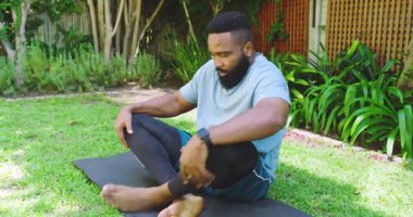 Afrikalı Amerikalı bir adam yemyeşil bahçedeki yoga minderi üzerinde meditasyon yapıyor, içsel sakinlik hissi yayıyor. yoga, meditasyon, sükunet, rahatlama, yeşillik, sağlık, farkındalık