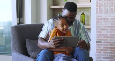 Afro-Amerikan ailesi tablet dağıtımına gülerek ve ekranı eğlencesine tıklatarak tepki veriyor. Aile, bağ, teknoloji, rahatlama, neşe, samimiyet, modern