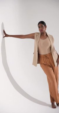 Dikey video: Kendine güvenen, şık kıyafetler içinde poz veren, stüdyoda zarafetle eğilen bir kadın. Moda, zarafet, tarz, portre, güven, cazibe