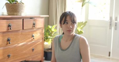 Asyalı kadın nefes alma ipuçlarını takip ediyor, ellerini göğsüne koyuyor ve karnını evdeki egzersiz paspasına koyuyor. Sağlık, rahatlama, farkındalık, dinginlik, iç mekan, doğal ışık, sakinlik.