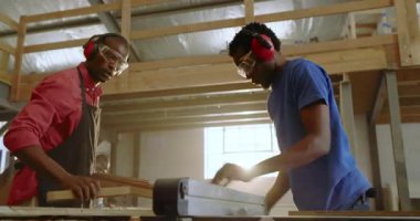 Testereye yaklaşıyoruz, Afro-Amerikalı zanaatkarlar atölyede tahta kesiyor, fotokopi çekiyor. Atölye, marangozluk, kereste, elektrikli aletler, takım çalışması, işçilik, sanayi