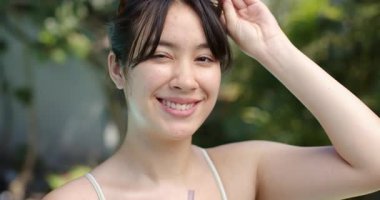 Susuzluk çeken, mayo giymiş, mor kavanozu yudumlayan, yenilenmek için havuz başında güneş gözlüğü kaldıran Asyalı bir kadın. Rahatlama, rahatlama, yaz, açık hava, sağIık, sükunet, gündelik