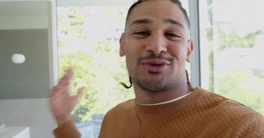 Merceğe uzanan, süveter ve kolye giyen adam gülümseyen, modern iç mekan gösteren kameraya konuşan. Vlogger, yaşam tarzı, minimalizm, iç mimari, açık hava, doğal ışık