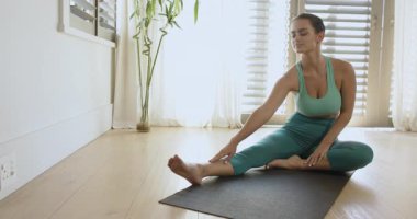 Ev oturumuna başlarken, kadın esnek olmak için siyah yoga minderinde vücut titreşimleriyle esneme hareketi yapıyor. Fitness, esneklik, sağIık, barışçıl, minimalist, dinginlik, egzersiz