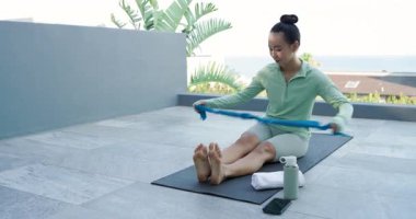 Mavi bantlı terasa adım atmak, paspas seren bir kadın, döngü bandı, çekirdek kuvveti için kürek çeken bir kadın. Zindelik, sağlık, açık hava, minimalist, güç, kararlılık, sağlık