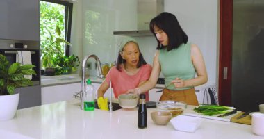 Musluğu çevirdikten sonra Çinli anne tava fırçaladı ve kızı mutfak adasına salata fırlattı. Aile, yerli, aşçı, yaşam tarzı, modern, canlı, bağlantı