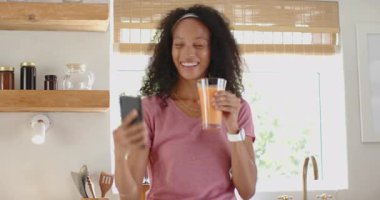 Mutfakta taze smoothie içen, şık giyinen ve sıradan giyinen bir kadın, evde. Sağlıklı, yaşam tarzı, teknoloji, beslenme, sağlık, zindelik