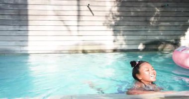 Mor mayo giyen kız tekmeliyor, havuzda yüzme kenarına doğru süzülüyor, kepçeyle yukarı çekiliyor, gülümsüyor. Çocuk, eğlence, coşku, neşe, açık hava, rahatlama, yaz