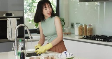 Asyalı anne ve kız musluğun sesini duyuyor, lavaboda sebzeleri duruluyor, yemek hazırlığı için otları doğruyor. Yemek, mutfak, yemek hazırlama, takım çalışması, yerli, modern, aile