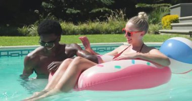 Çeşitli çiftler akıllı telefonları kadın gibi sıçratan bir adamla şakalaşıyor. Havuzda pembe şamandırada uzanan bir kadın gibi. Rahatlama, rahatlama, açık hava, canlı, neşeli, dostluk, yaşam tarzı.