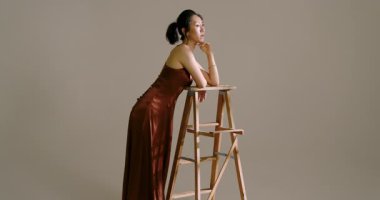 Asyalı kadın modellere rehberlik eden eğimli ışıklı bantlar tahta merdiven dayayıp stüdyoda poz veriyor. Zarafet, sofistike, minimalizm, moda, tefekkür, güzellik, sükunet