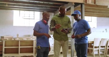 Afro-Amerikalı marangozlar, mağaza ve fotokopi alanındaki müdürle birlikte tablet üzerinde dolap planlarını gözden geçiriyorlar. İşbirliği, işçilik, doğruluk, takım çalışması, endüstriyel, modern, üretkenlik