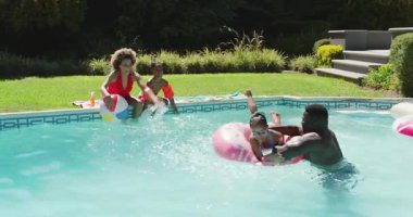 Çeşitli aileler çizgili plaj topunu kaldırıyor, tüplerle bilardo oynuyor, su sıçratıyor, gülüyor. Aile, havuz başı, yaz tatili, boş zaman, açık hava, neşe, neşe