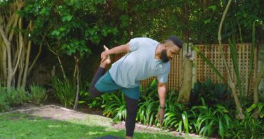 Bahçedeki yoga minderinde canlı yeşil yapraklarla yoga yapan Afrikalı Amerikalı bir adam. Yoga, fitness, rahatlama, farkındalık, doğa, açık hava, sağlık