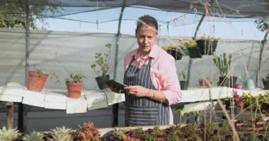 Bahçıvan seradaki bitkilerle ilgilenirken tablet kullanıyor. Bahçıvanlık, bahçıvanlık, teknoloji, tarım, tarım