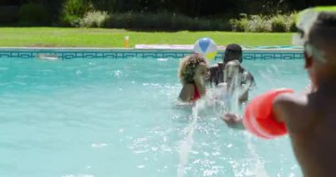 Çeşitli aileler plaj topu atıyorlar, çocukları eğlence için evlerinin havuzuna götürüyorlar. Aile, arka bahçe, su, eğlence, eğlence, yaz, oyuncu.