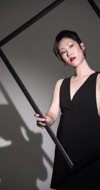 Dikey video: Siyah elbiseli zarif kadın çerçeveli poz veriyor, modern moda tarzını sergiliyor. zerafet, cazibe, trend, şık, sofistike, tarz