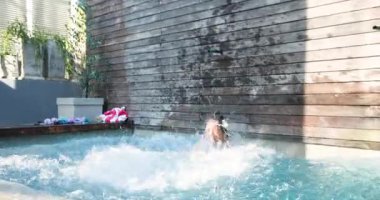 Asyalı anne ve Afrikalı Amerikalı kız havuza geliyor, pembe şamandırayla yüzmeyi öğreniyorlar. Aile, eğlence, eğlence, su, yaz, kaynaşma, oyun.