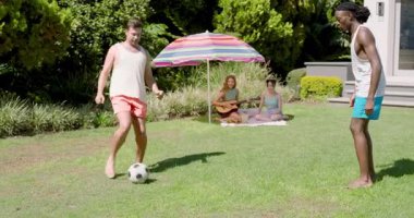 Çeşitli arkadaşlar arka bahçede şemsiyenin altına battaniye serip gitar hokkabazlığı yapıyorlar. Gündelik, açık hava buluşması, eğlence, uyum, canlı yaşam tarzı, eğlence.