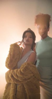 Dikey video: Stüdyoda dramatik stüdyo ışıkları altında şık kıyafetler giyen kadınlar güven içinde poz veriyor. Moda, güven, zarafet, cazibe, tarz, portre