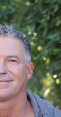 Dikey video: Gülümseyen olgun bir adam yemyeşil yemliğin yakınında güneşli bir sabahın tadını çıkarıyor. Güneş ışığı, doğa, mutluluk, rahatlık, rahatlama, kıdemli