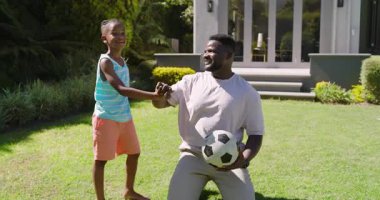 After tapping ball, Diverse father and son practicing dribbling, passing soccer ball in backyard. Athletic, teamwork, leisure, fitness, outdoor, energetic, playful