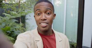 Kamerayı sürgülü kapıdan tutan, eğrelti otlarını gösteren ve el sallayan Afrikalı Amerikalı adamı selamlıyorum. Vlogger, outdoor, modern, yaşam tarzı, canlı, neşeli, kentsel