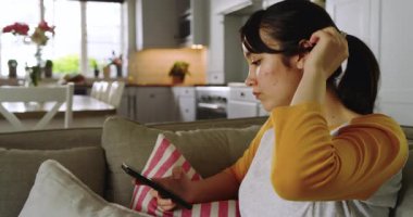 Yastığın üzerinde akıllı telefon tespit etmek, Asyalı bir kadının onu alıp koltukta mesajları kontrol etmesi, fotokopi çekmek. Teknoloji, rahatlama, gündelik, ev içi, yaşam tarzı, dijital, konfor