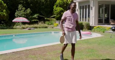 Çeşitli arkadaşlar oyuna sarı top atarak ve arka bahçedeki havuzda raketlerle oynaşarak başlıyor. Açık hava eğlencesi, eğlence, coşku, gündelik, arkadaşlık, yaz, aktivite