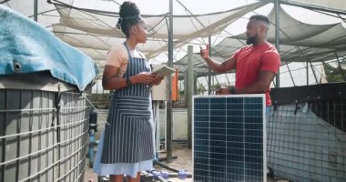 Afrika kökenli Amerikalı kadın ve erkek serada güneş paneli kurulumunu tartışıyor. Sürdürülebilirlik, enerji, yenilenebilirlik, işbirliği, takım çalışması, çevre