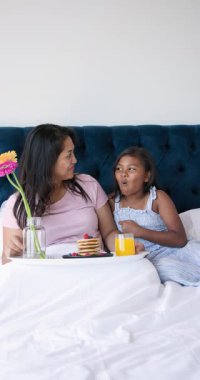 Dikey video: Anne ve kızı yatakta kahvaltı yapıyor, krep ve portakal suyu paylaşıyorlar. Aile, bağ, sabah, rahat, hafta sonu, rahatlama