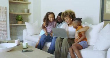 Farklı aile dizüstü bilgisayarlarını kanepede paylaşıyor, oğlan katılıyor, kız eğiliyor, anne daktilo ediyor ve işaret ediyor. Aile, birliktelik, etkileşim, bağlanma, rahatlık, rahatlık, mutluluk.