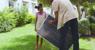 Afrikalı Amerikalı baba ve kızı bahçede güneş panelini inceliyor. Sürdürülebilirlik, teknoloji, babalık, bağlanma, yenilenebilir enerji