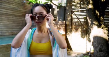 Orta yaşlı Asyalı bir kadın, havuzda çizgili örtüyü düzeltiyor. Kaplumbağa kabuğu güneş gözlüğü takıyor. Yaşam tarzı, eğlence, moda, açık hava, sıcaklık, dinginlik, gündelik