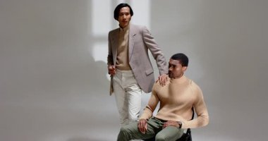 Diverse male coworkers entering studio touching colleague shoulder and adjusting blazer for styling. Professional, collaboration, fashion, minimalist, business, modern, camaraderie