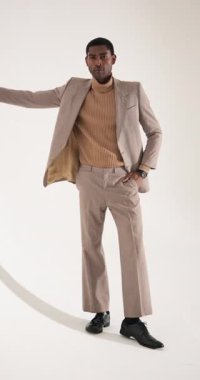 Dikey video: Stüdyoda beyaz duvara karşı poz veren şık takım elbiseli kendine güvenen adam. Moda, mankenlik, erkek giyim, zarafet, resmi giyim, özgüven.