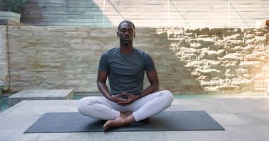 Siyah yoga minderi üzerinde meditasyon yapan Afrikalı Amerikalı bir adam modern mekanda sakin bir atmosferi benimsiyor. Meditasyon, sükunet, farkındalık, sağlık, rahatlama, dinginlik, odaklanma.